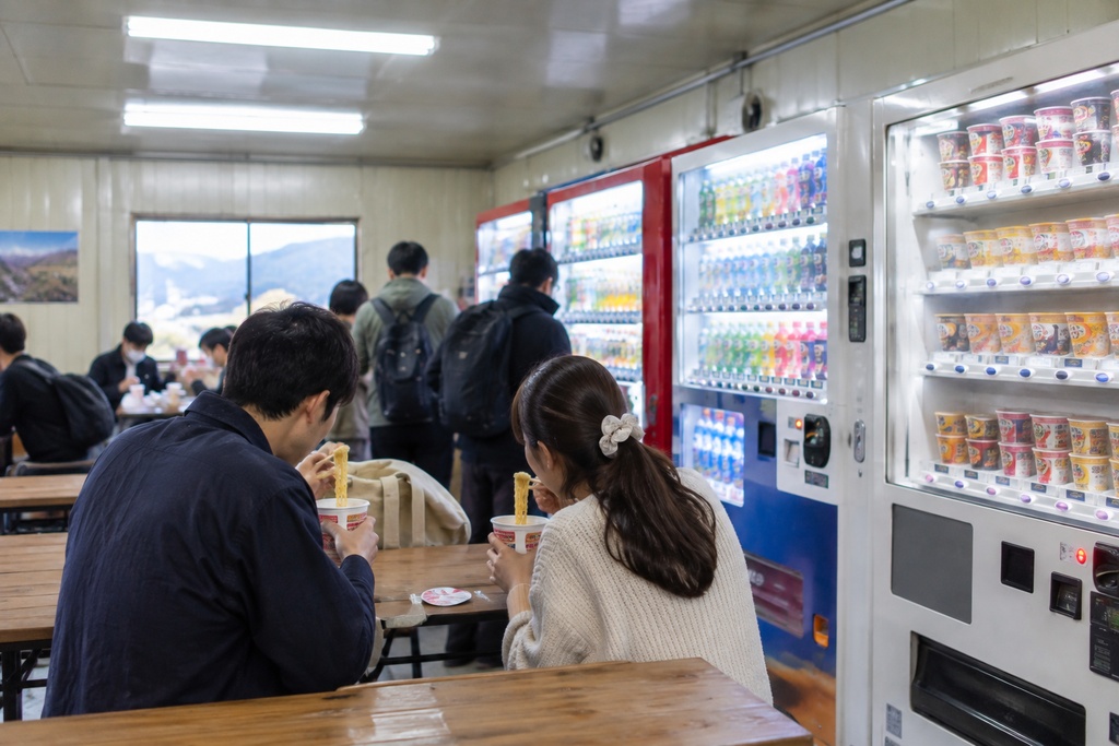 並んでいる自動販売機の前でカップラーメンを食べている若夫婦