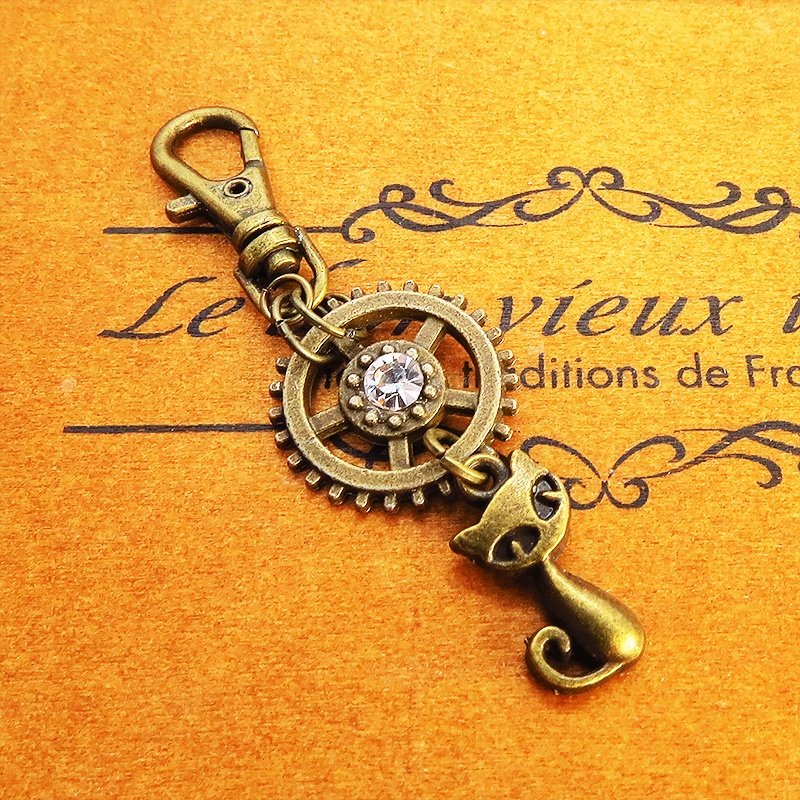 アンティークゴールド 猫と歯車を組合せた可愛いキーホルダー スワロフスキー・クリスタル バッグチャーム ファスナーチャーム