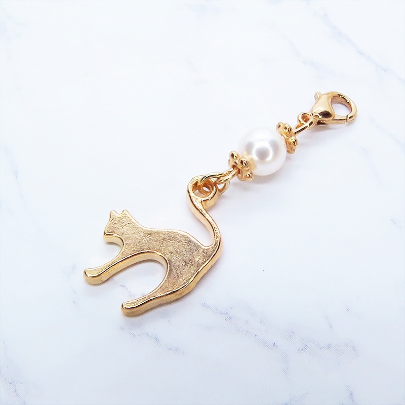 マスクチャーム マットゴールドの跳ね猫モチーフとスワロフスキーパール(クリスタルホワイト)のチャーム キーホルダー