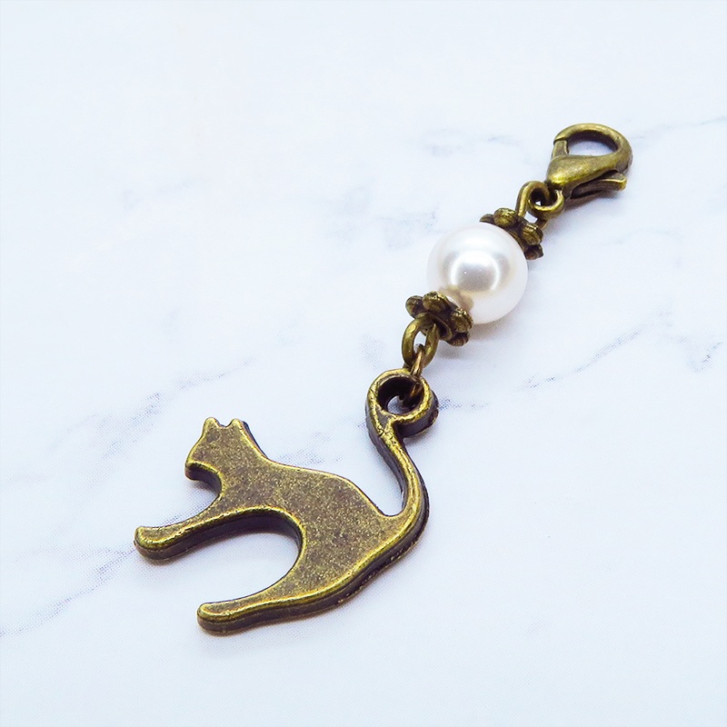 マスクチャーム アンティークカラーの跳ね猫モチーフとスワロフスキーパール(クリスタルホワイト)のチャーム キーホルダー
