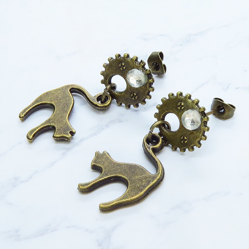 アンティークゴールドの跳ね猫モチーフと歯車のスチームパンク風スタッドピアス クリスタルガラス