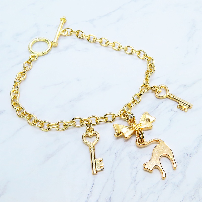 マットゴールドの跳ね猫シルエットモチーフとリボンに鍵が連なるブレスレット