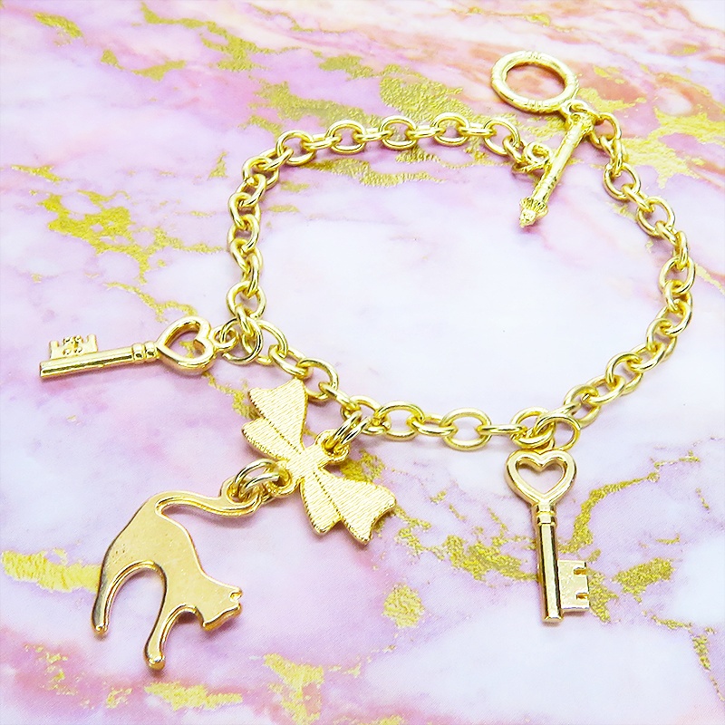 マットゴールドの跳ね猫シルエットモチーフとリボンに鍵が連なるブレスレット