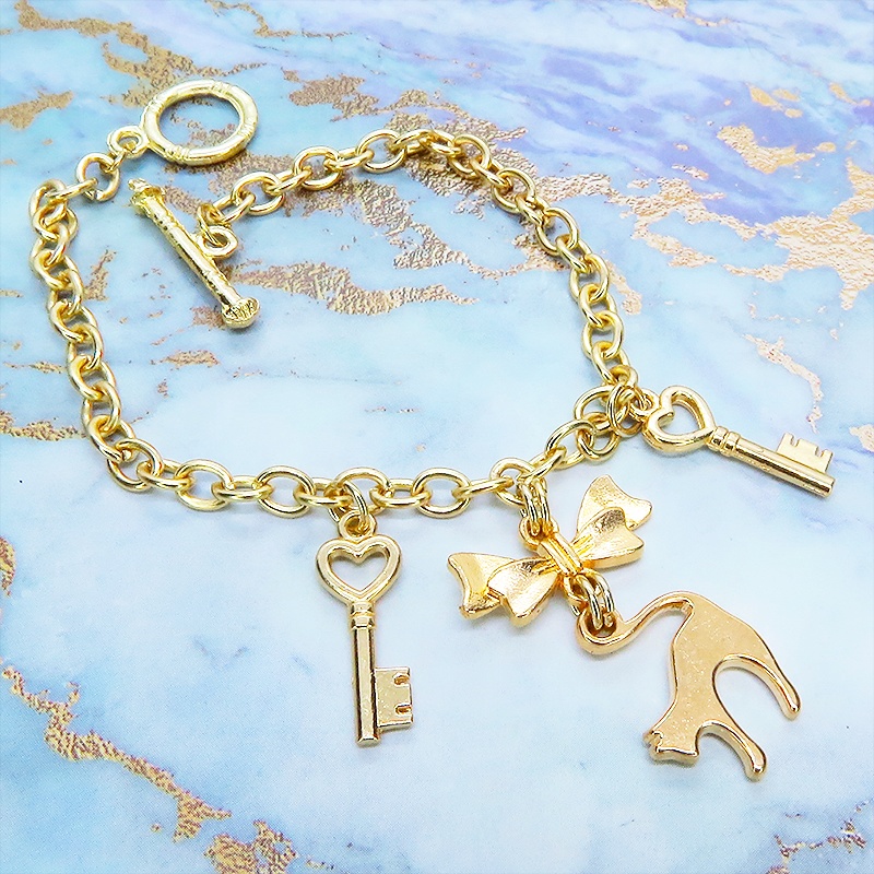 マットゴールドの跳ね猫シルエットモチーフとリボンに鍵が連なるブレスレット