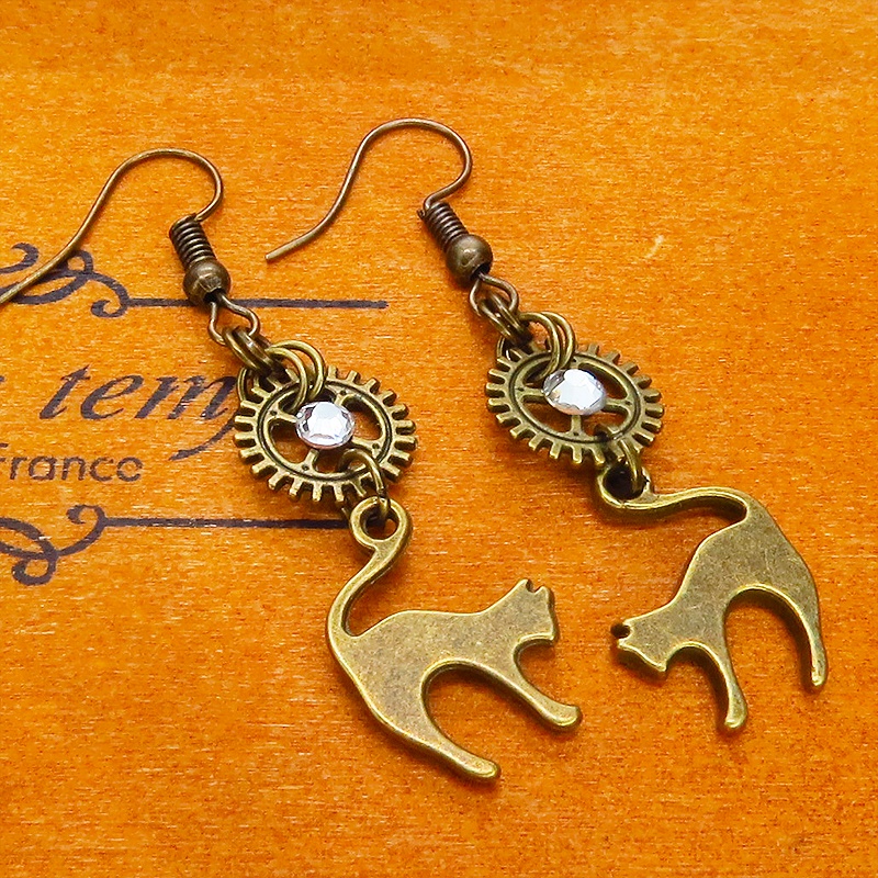 アンティークゴールド 跳ね猫モチーフと歯車を組合せたシンプルなピアス クリスタルガラス