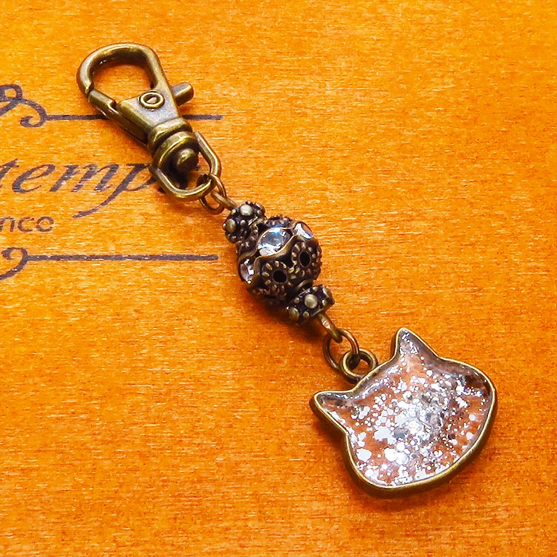 アンティークゴールド 猫フェイスモチーフのクリアカラーレジンのキーホルダー ラインストーン入りメタルビーズ 金具変更可